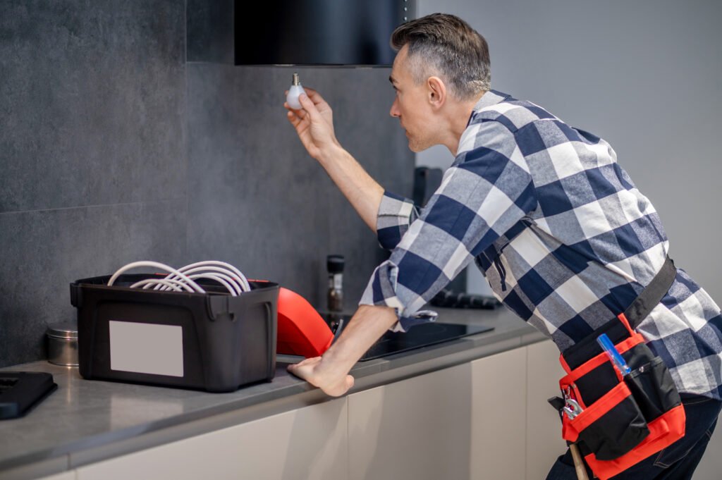 Service de maintenance technique rapide et efficace avec Homely pour vos locations Airbnb Homme effectuant une maintenance technique dans une location Airbnb, en remplaçant une ampoule, avec l'assistance de Homely